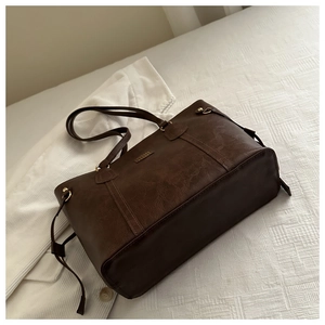 Detail of the high-quality leather texture and golden metal logo on the brown tote bag