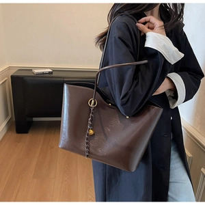 Macro detail of dark brown glossy leather tote bag with braided charm and gold ball
