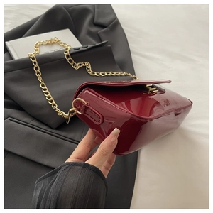 Gros plan du sac en cuir verni bordeaux avec bandoulière chaîne dorée et fermoir métal