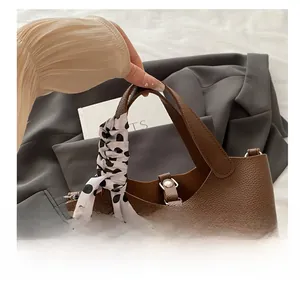 Close-up of brown litchi leather bucket bag handle wrapped with polka dot silk scarf