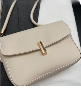 Close-up of minimalist cream white leather crossbody bag with golden metal buckle and strap