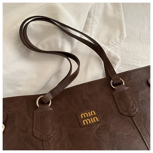 Detail of vintage brown leather tote bag showing gold logo and grain texture