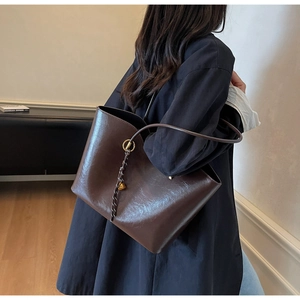 Detail of dark brown glossy leather tote bag with a golden bell and woven pendant