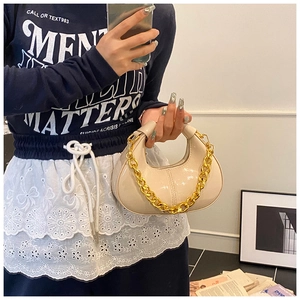 Detail of cream glossy hobo bag with thick gold chain strap worn by a model
