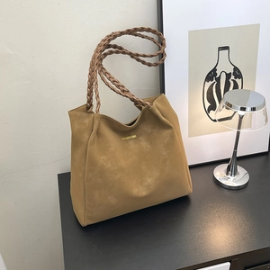 Brown large capacity tote bag with braided shoulder straps and gold logo on black table