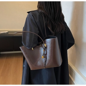 Detail of dark brown glossy leather tote bag with metallic bell charm on slender shoulder strap