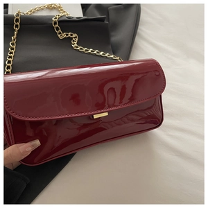 Détail du sac en cuir verni bordeaux brillant avec une boucle dorée élégante
