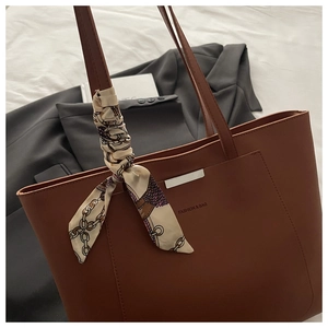 Brown leather tote bag featuring a silk scarf accessory and metal decorative bar details