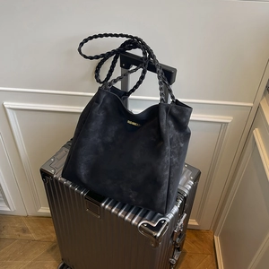 Large black matte tote bag with woven handles and gold logo on a silver suitcase