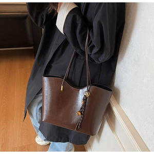 Close-up of a vintage dark brown tote bag with glossy leather texture and braided pendant