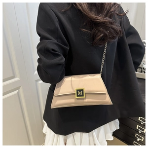 Close-up of beige trapezoid crossbody bag with gold chain strap and M logo buckle
