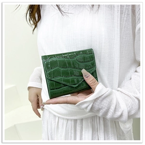 Close-up of green crocodile texture patent leather envelope clutch bag held by model