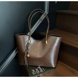Macro view of dark coffee tote bag featuring sleek PU texture and woven charm detail