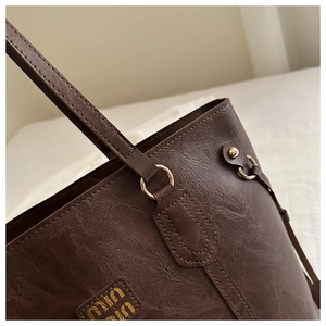 Detail shot of deep brown leather tote bag with Miu Miu logo and gold hardware