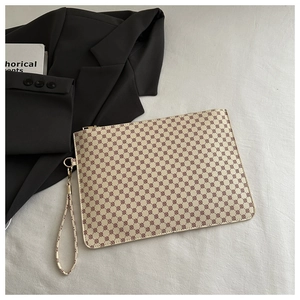 Dettaglio pochette a busta con motivo geometrico e cinturino da polso su una scrivania minimalista