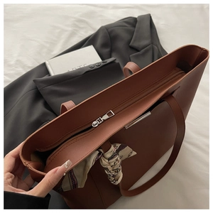 Detail of caramel leather tote bag with silk scarf and zipper closure on fabric