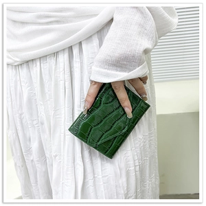 Close-up of deep green crocodile embossed patent leather envelope clutch bag held by a model