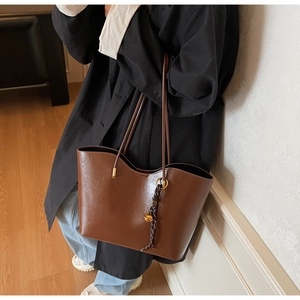 Brown faux leather tote bag with woven charm shown from side view on model shoulder