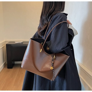 Brown leather tote bag featuring a gold bell pendant shown on a model's shoulder