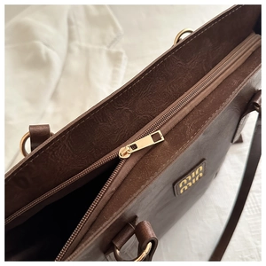 Detail of the golden metal logo and zipper closure on a brown textured tote bag
