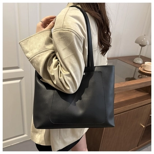 Side view of a large black matte tote bag worn by a model in a warm indoor setting