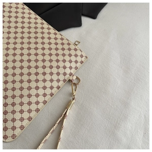 Dettaglio pochette crema con motivo a quadrifoglio rosso-marrone e hardware dorato