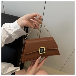 Close-up of brown leather bag featuring a gold square buckle with a signature M logo