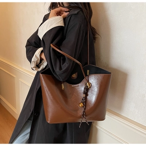 Detail view of large dark brown leather tote bag with braided charm and gold hardware