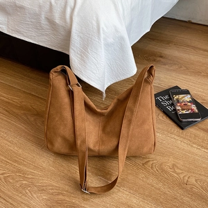 Large brown canvas tote bag with adjustable strap on a light wood floor background