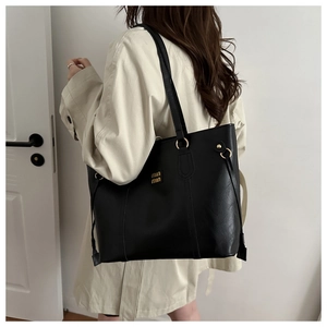 Close-up of black lychee texture leather tote bag featuring gold logo and side drawstring
