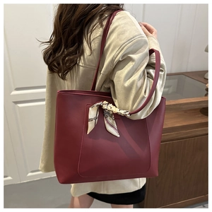 Detail of dark red leather tote bag featuring a decorative silk scarf on the handle