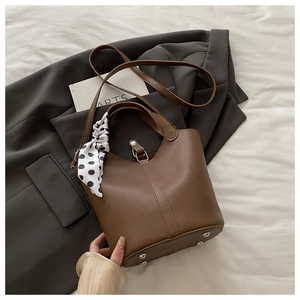 Detail of brown litchi pattern leather bucket bag with decorative polka dot scarf and metal studs