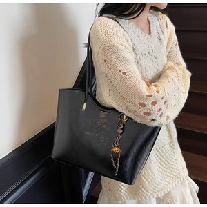 Glossy black PU tote bag with metal bell charm and braided ribbon on casual model