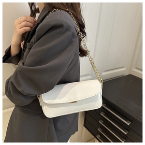 Détail d'un sac bandoulière en cuir blanc brillant avec chaîne dorée sur blazer gris