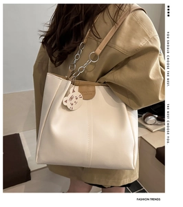 Detail of off-white tote bag featuring brown leather trim and a tiger charm accent