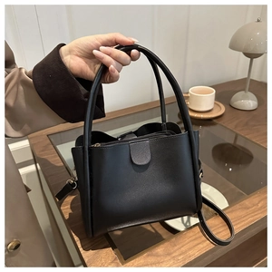 Detail view of the black leather bucket bag with top handles and a secure zipper closure