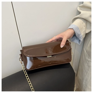 Gros plan détaillé du sac à bandoulière en cuir verni marron foncé et chaîne dorée