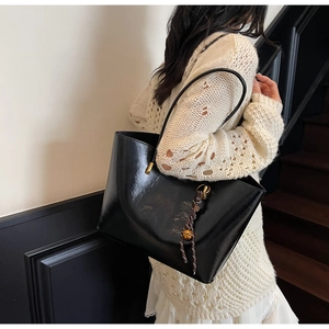 Detail of black glossy tote bag with minimalist design and woven rope pendant charm