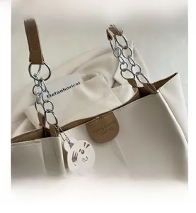 Detail of cream tote bag with brown leather patch and cute cat charm attachment