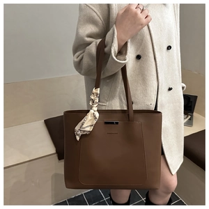 Close-up of brown leather tote bag with fashion lettering and silk scarf on handle