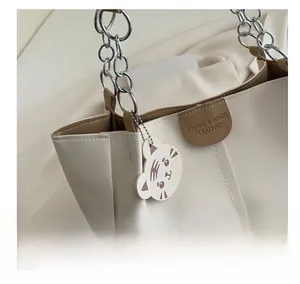 Detail of off-white tote bag with silver chain handle and cute tiger charm accessory