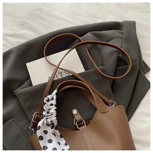 Brown lychee leather bucket bag with polka dot scarf on clean white bedding