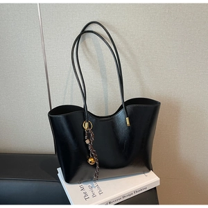 Detail of black glossy tote bag with slim shoulder strap and golden ball pendant