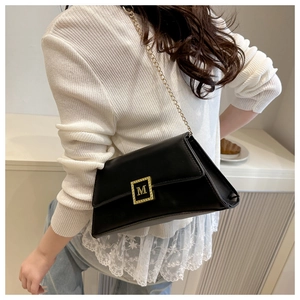Detail of a black leather crossbody bag featuring a gold M logo buckle and chain strap