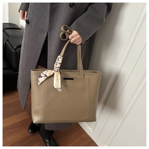 Close-up of khaki leather tote bag with metal bar detail and decorative printed silk scarf