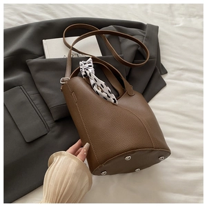 Detail of brown lychee grain leather bucket bag with silk scarf and metal base studs