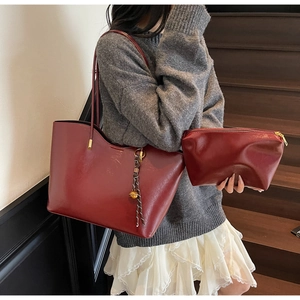 Detail of wine red leather tote bag with braided knot charm on a grey sweater