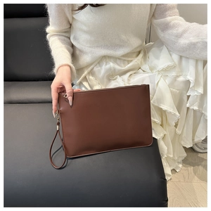 Dettaglio della pochette in pelle marrone scuro con cinturino da polso e modella
