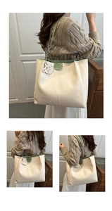Detail of minimalist cream tote bag with green trim and metal chain strap