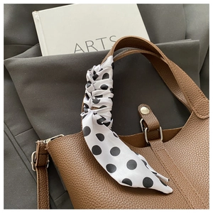 Close-up of a black and white polka dot silk scarf tied on a brown leather bucket bag
